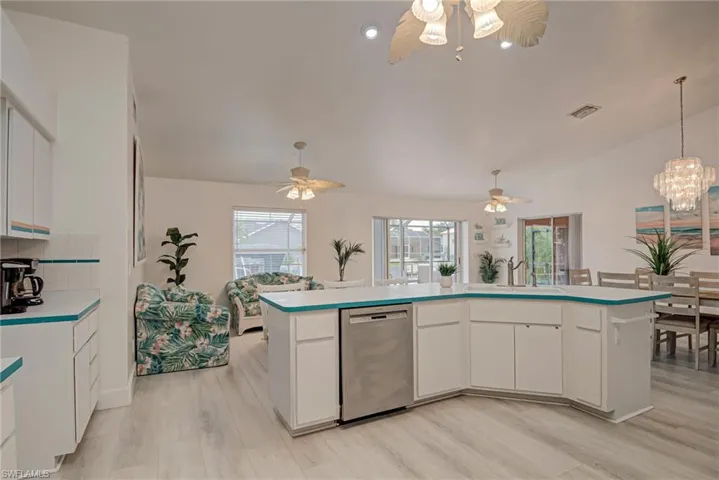 Kitchen with white cabinetry, stainless steel dishwasher, a chandelier, a center island with sink, and lofted ceiling