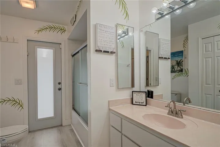 Bathroom with vanity, enclosed tub / shower combo, light wood-type flooring, and a closet
