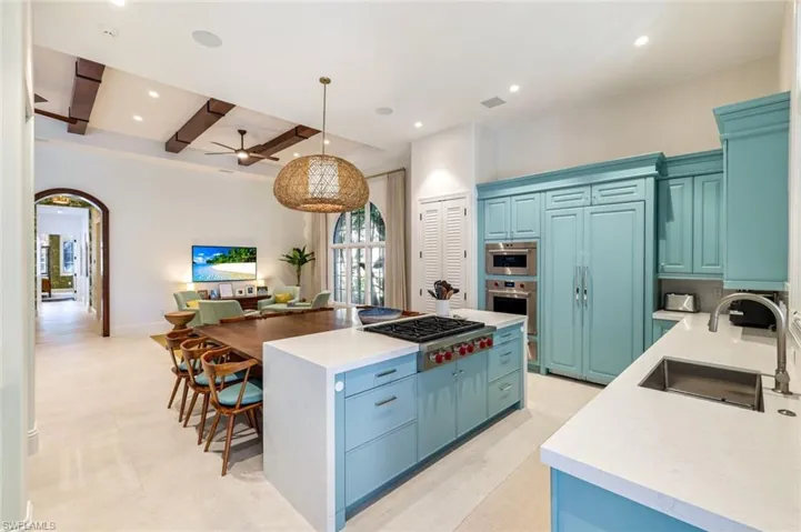 Kitchen with light stone countertops, blue cabinets, hanging light fixtures, arched walkways, and beam ceiling