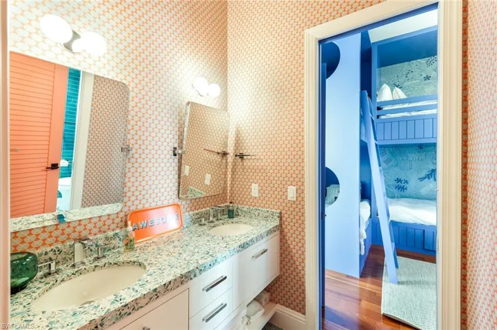 Full bath featuring wallpapered walls, double vanity, dark wood-style flooring, and connected bathroom