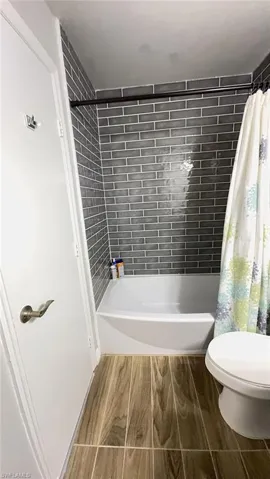Bathroom featuring a full tub with shower, subway tile surround, wood-finish tile flooring, and a white toilet