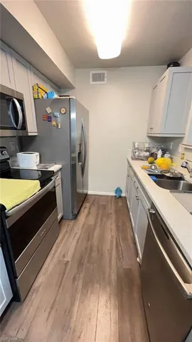 Galley kitchen featuring wood-finish flooring, light grey cabinetry, stainless steel appliances, and light-toned countertops