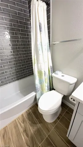 Bathroom featuring a white bathtub, dark gray subway tile surround, wood-finish flooring, a white toilet, and a white vanity with a light-colored countertop