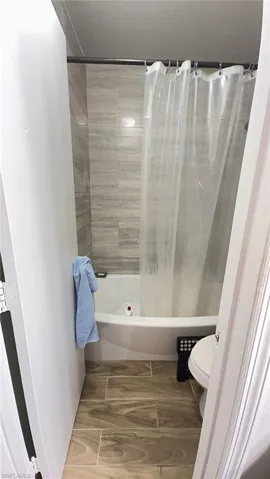 Bathroom featuring a white bathtub, wood-finish floor tiles, and grey horizontal wall tiling