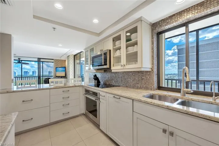 Kitchen featuring backsplash, light stone counters, white cabinets, glass insert cabinets, and stainless steel appliances