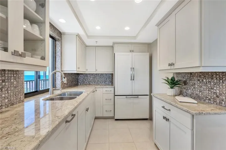 Kitchen with light stone countertops, paneled built in fridge, light tile patterned flooring, recessed lighting, and a raised ceiling