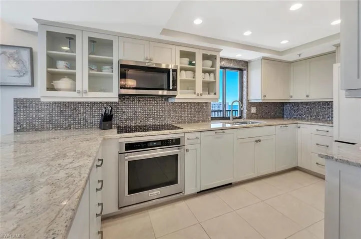 Kitchen with appliances with stainless steel finishes, light stone countertops, backsplash, light tile patterned floors, and a raised ceiling