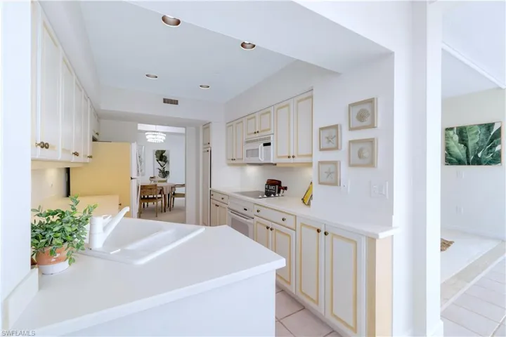 Kitchen featuring kitchen peninsula, white appliances, sink, cream cabinets, and light tile patterned flooring