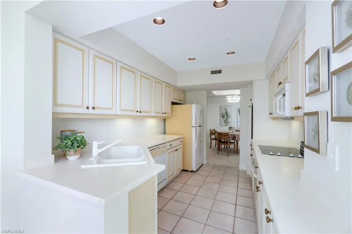 Kitchen with sink, an inviting chandelier, kitchen peninsula, white appliances, and light tile patterned floors
