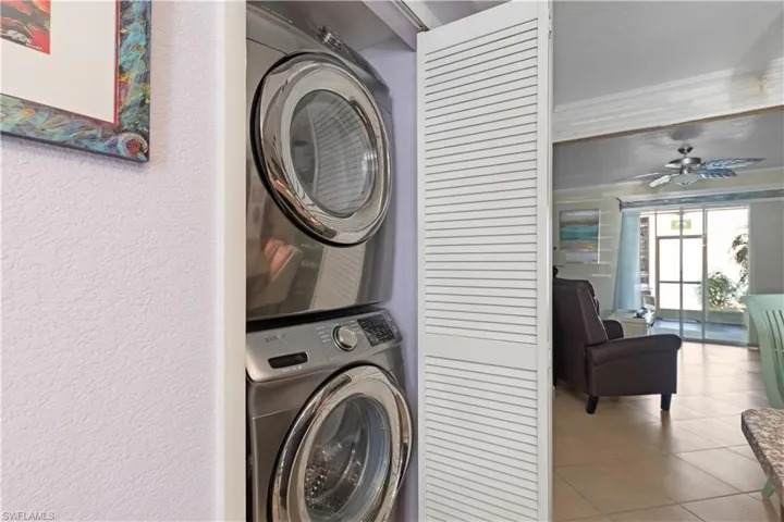Laundry area featuring stacked washer and clothes dryer, light tile patterned floors, and a ceiling fan