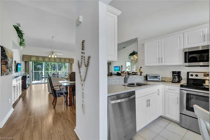 Kitchen with stainless steel appliances, vaulted ceiling, sink, light hardwood / wood-style floors, and white cabinetry