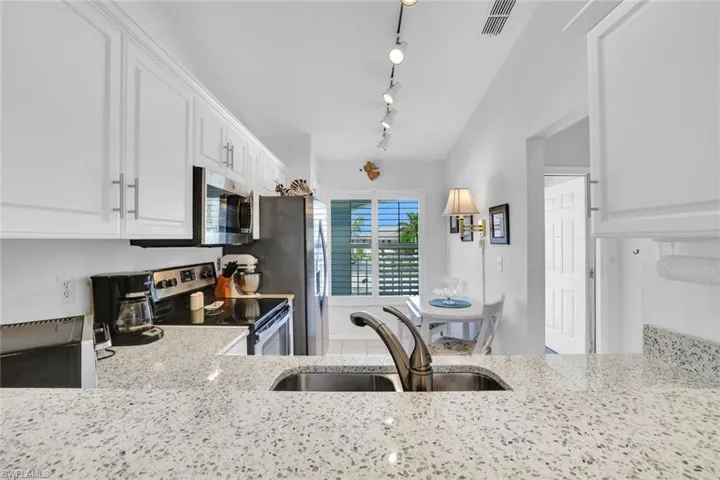 Kitchen featuring appliances with stainless steel finishes, light stone counters, sink, white cabinets, and lofted ceiling