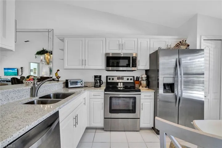 Kitchen with white cabinetry, sink, stainless steel appliances, lofted ceiling, and light tile patterned floors