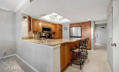 Kitchen with wood finish cabinetry, a peninsula, stainless steel appliances, a kitchen breakfast bar, and light stone counters