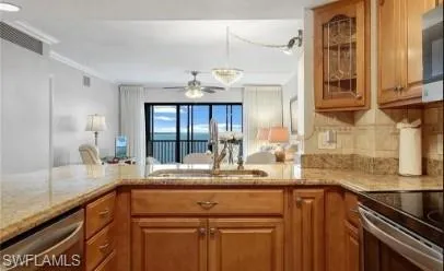 Kitchen featuring glass fronted cabinets, light stone counters, wood finish cabinets, stainless steel appliances, and a ceiling fan