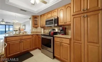 Kitchen with a ceiling fan, stainless steel appliances, glass fronted cabinets, hanging light fixtures, and a raised ceiling