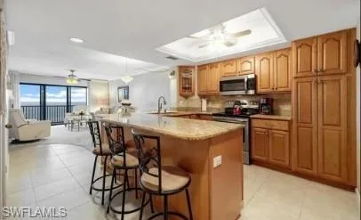 Kitchen featuring a ceiling fan, wood finish cabinetry, stainless steel appliances, a kitchen breakfast bar, and open floor plan