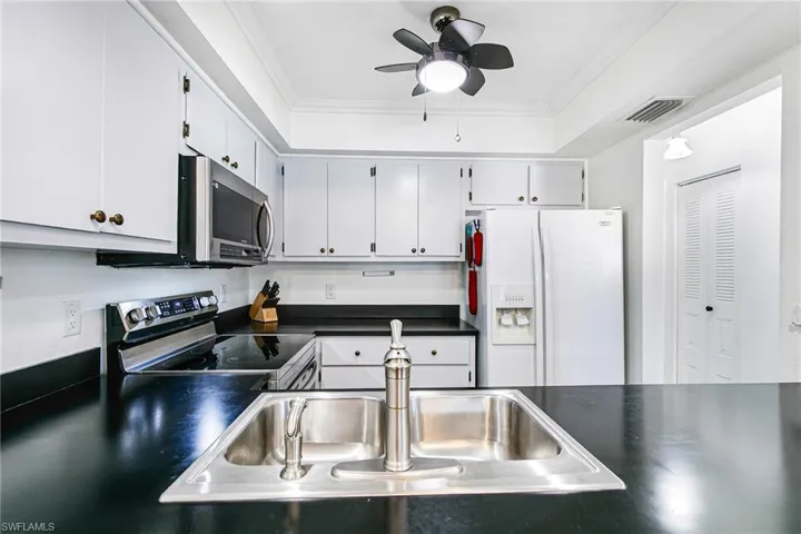Kitchen with dark countertops, appliances with stainless steel finishes, ornamental molding, a ceiling fan, and a tray ceiling