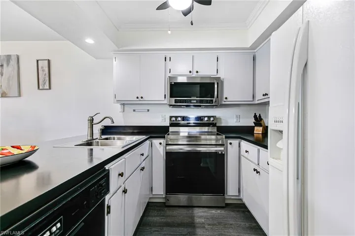 Kitchen with appliances with stainless steel finishes, ornamental molding, dark countertops, dark wood-style flooring, and a ceiling fan