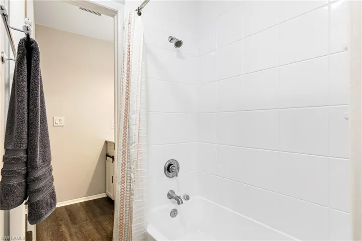 Full bath with shower / tub combo, vanity, and dark wood-style flooring