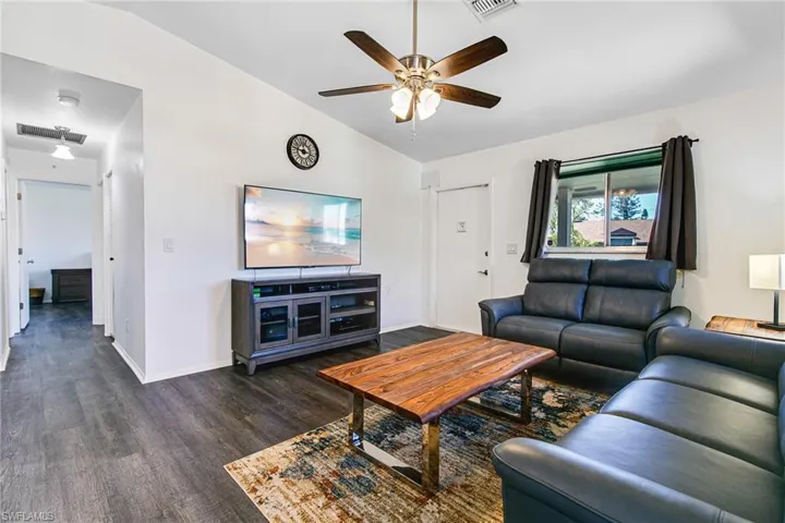 Living room featuring vaulted ceiling, dark wood-style floors, and a ceiling fan