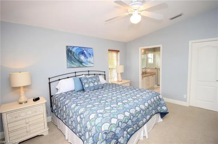 Carpeted bedroom with lofted ceiling, connected bathroom, and ceiling fan