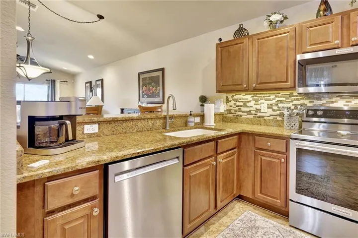 Kitchen with stainless steel appliances, sink, kitchen peninsula, light stone counters, and lofted ceiling