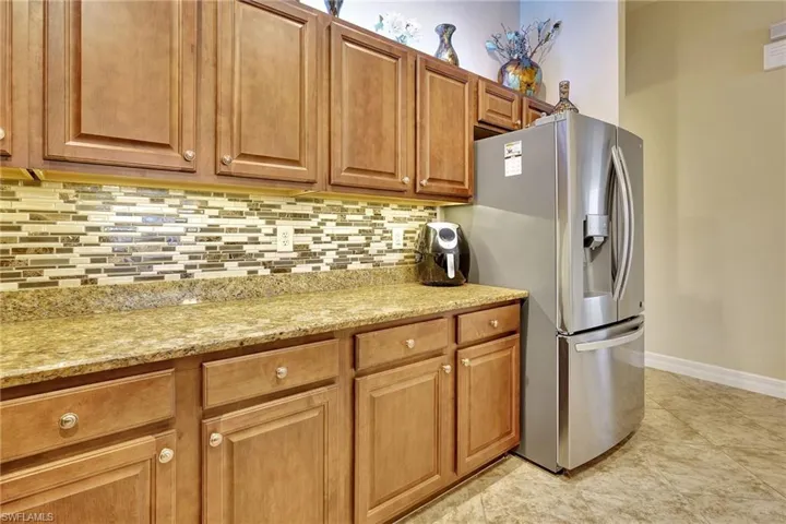 Kitchen featuring backsplash, light stone counters, stainless steel fridge, and light tile patterned floors
