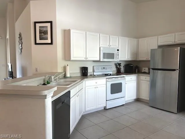 Kitchen featuring kitchen peninsula, white appliances, white cabinetry, and sink
