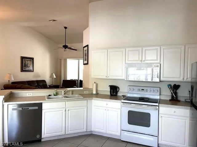 Kitchen with white appliances, ceiling fan, sink, white cabinetry, and light tile patterned flooring