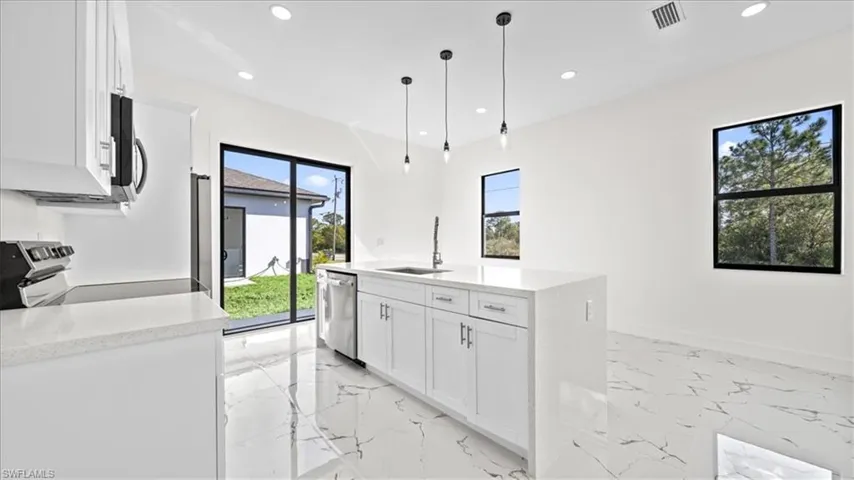 Kitchen featuring white cabinetry, light stone countertops, decorative light fixtures, and stainless steel appliances