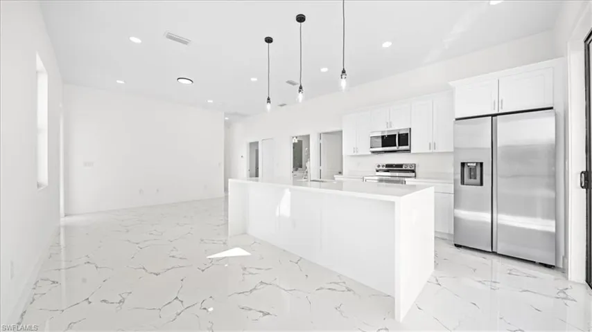 Kitchen with stainless steel appliances, white cabinets, decorative light fixtures, a center island with sink, and light marble finish flooring