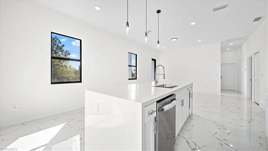 Kitchen with white cabinets, hanging light fixtures, light stone counters, stainless steel dishwasher, and light marble finish floors