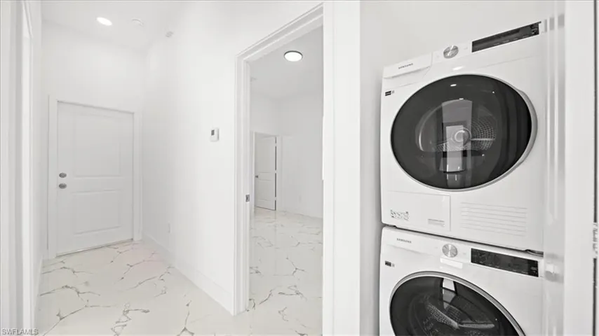 Laundry area with stacked washer and dryer, light marble finish floors, and recessed lighting