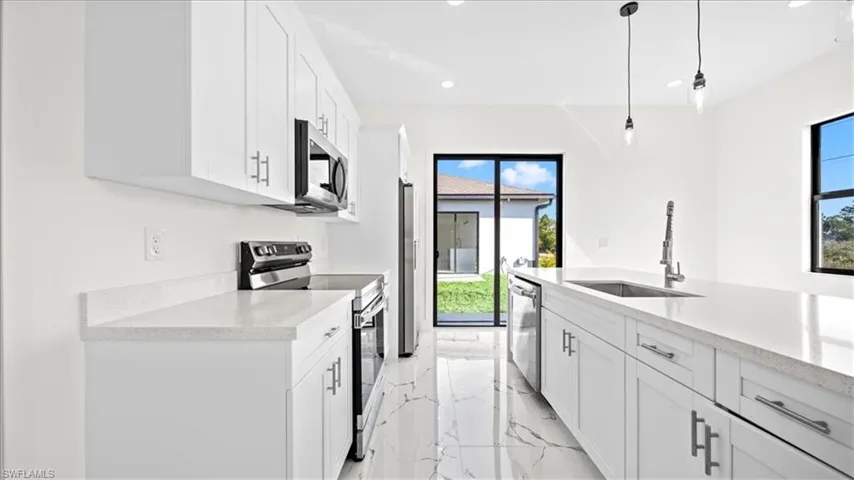 Kitchen with stainless steel appliances, white cabinetry, light stone countertops, light marble finish floors, and decorative light fixtures