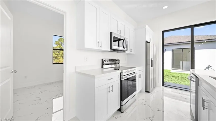 Kitchen with stainless steel appliances, light marble finish floors, white cabinetry, light stone countertops, and recessed lighting
