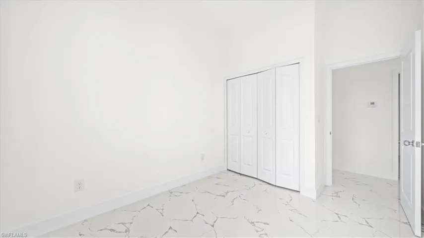 Unfurnished bedroom featuring light marble finish floors, a closet, and a high ceiling