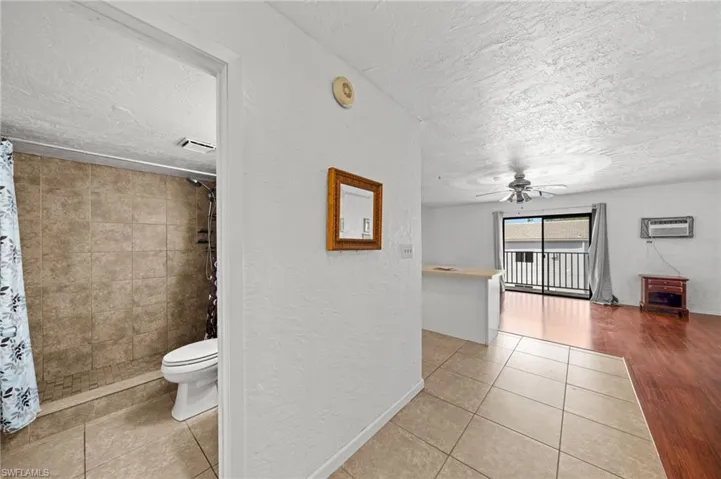 Bathroom with a textured ceiling, a textured wall, a shower stall, light tile patterned floors, and ceiling fan