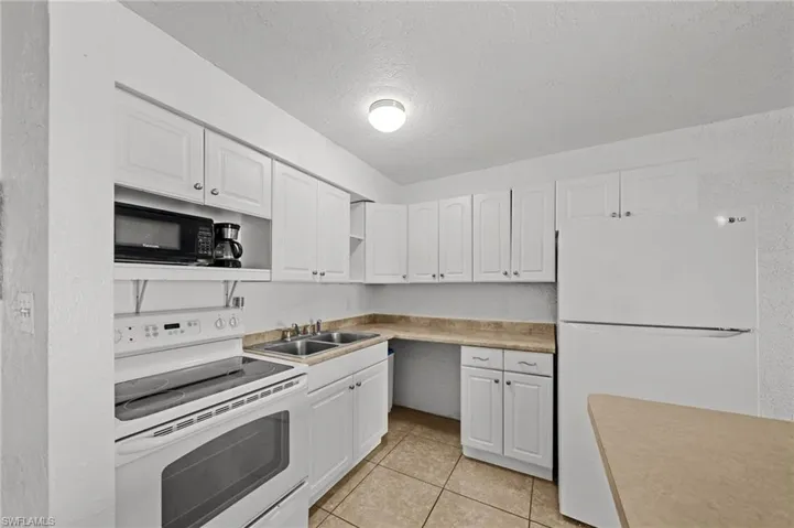 Kitchen featuring white appliances, a textured ceiling, open shelves, white cabinetry, and light tile patterned flooring