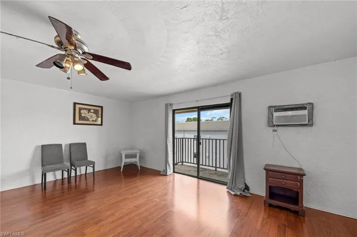 Living area with a textured wall, wood finished floors, a textured ceiling, a ceiling fan, and a wall mounted air conditioner