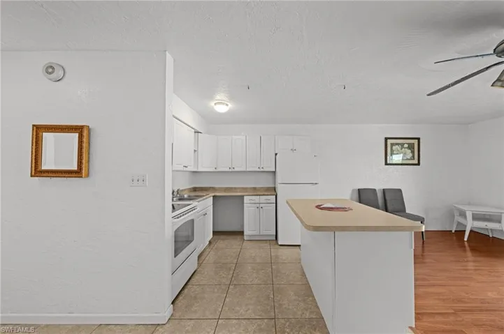 Kitchen featuring white cabinets, white appliances, a textured wall, light countertops, and a textured ceiling