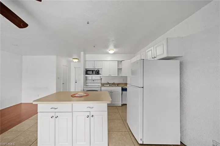 Kitchen featuring white appliances, a textured wall, white cabinetry, light tile patterned flooring, and open shelves