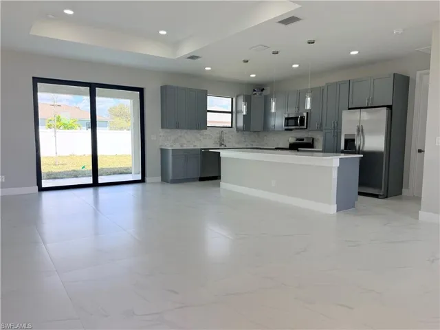 Kitchen featuring stainless steel appliances, gray cabinetry, a center island, light countertops, and decorative light fixtures