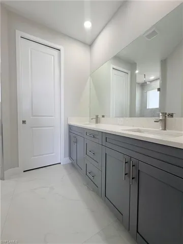 Full bathroom with double vanity, light marble finish floors, and recessed lighting