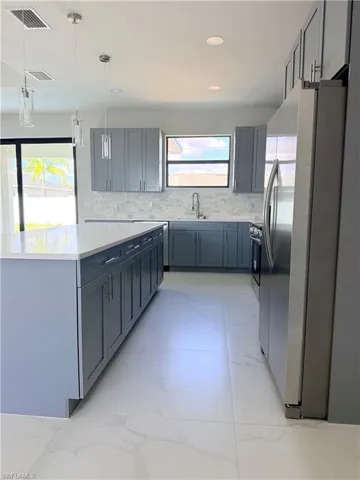 Kitchen featuring stainless steel appliances, gray cabinets, backsplash, and pendant lighting
