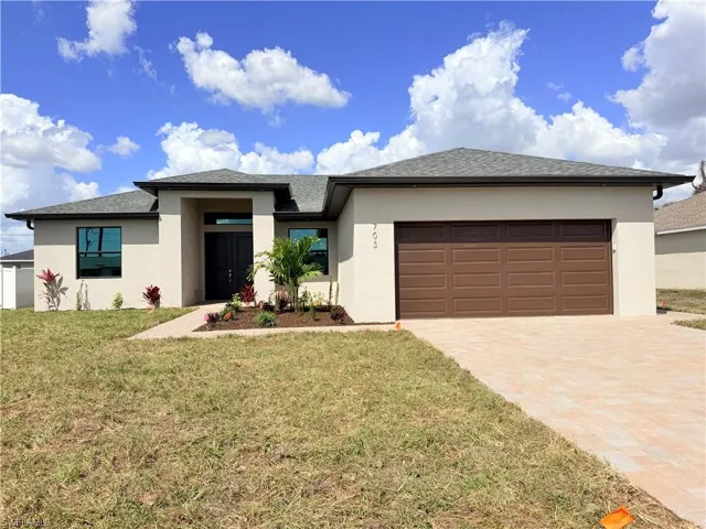 Prairie-style home with stucco siding, a garage, a front yard, and driveway
