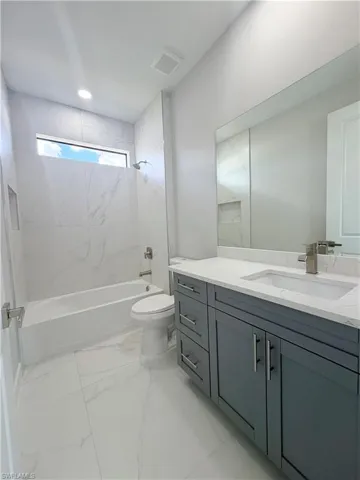 Bathroom featuring vanity, shower / washtub combination, and light marble finish floors