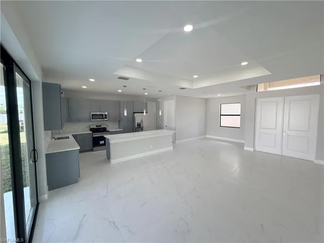 Kitchen featuring gray cabinetry, open floor plan, stainless steel appliances, a center island, and backsplash