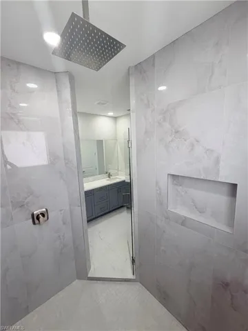 Bathroom featuring vanity, tile walls, recessed lighting, a tile shower, and light marble finish floors