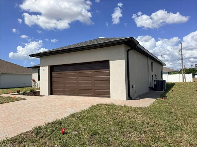 View of side of home with a yard, stucco siding, an attached garage, and decorative driveway